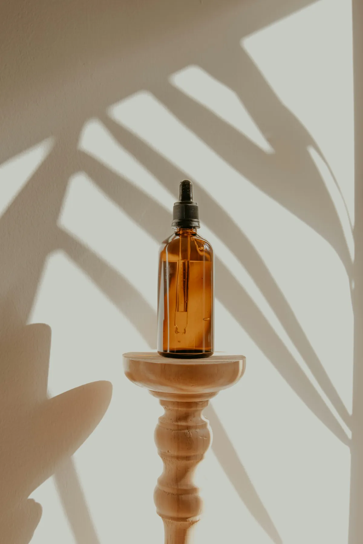 Frasco âmbar de sérum sobre pedestal com sombra de folhagem