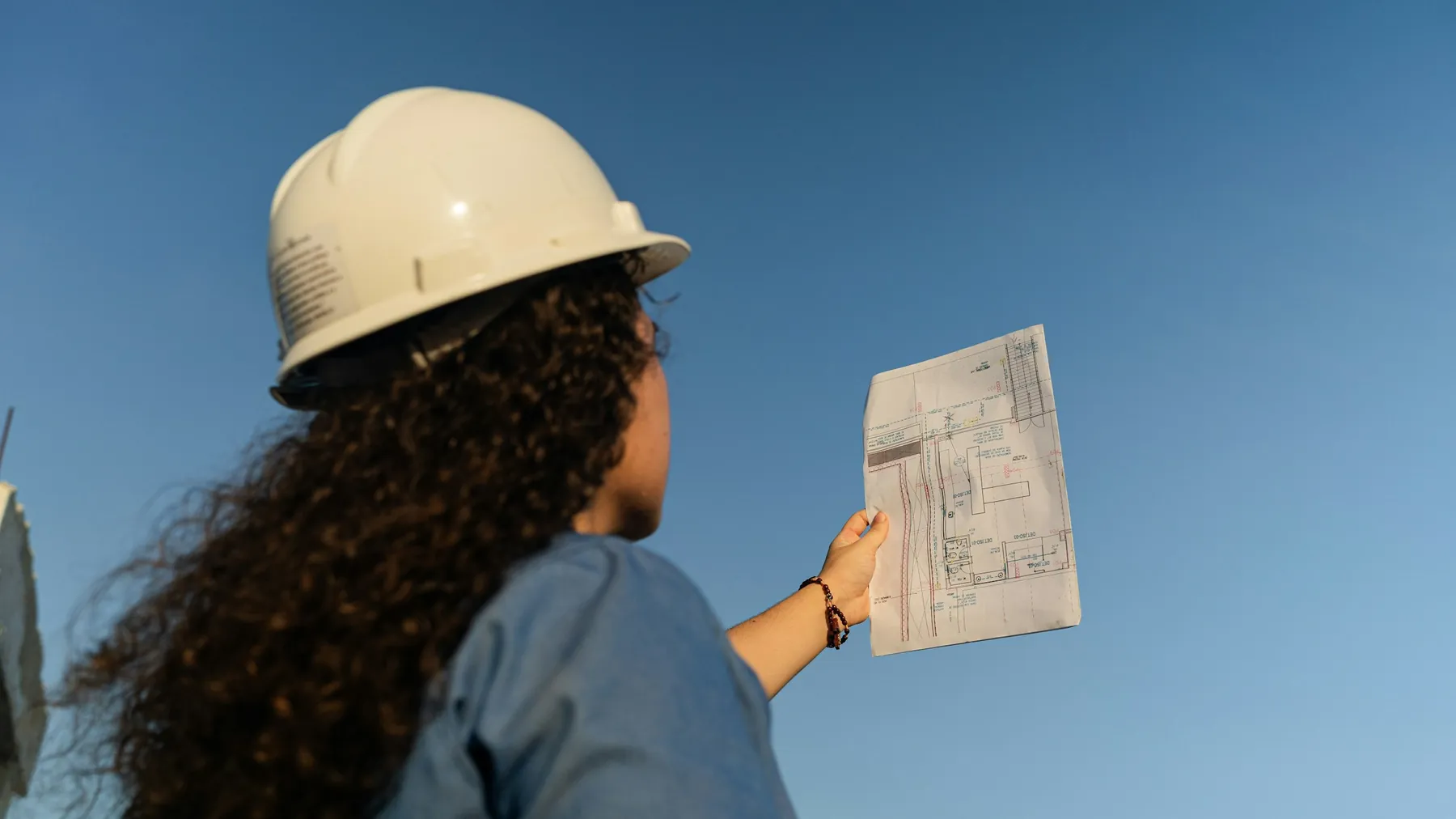 Engenheira de capacete analisando a planta da obra contra o céu